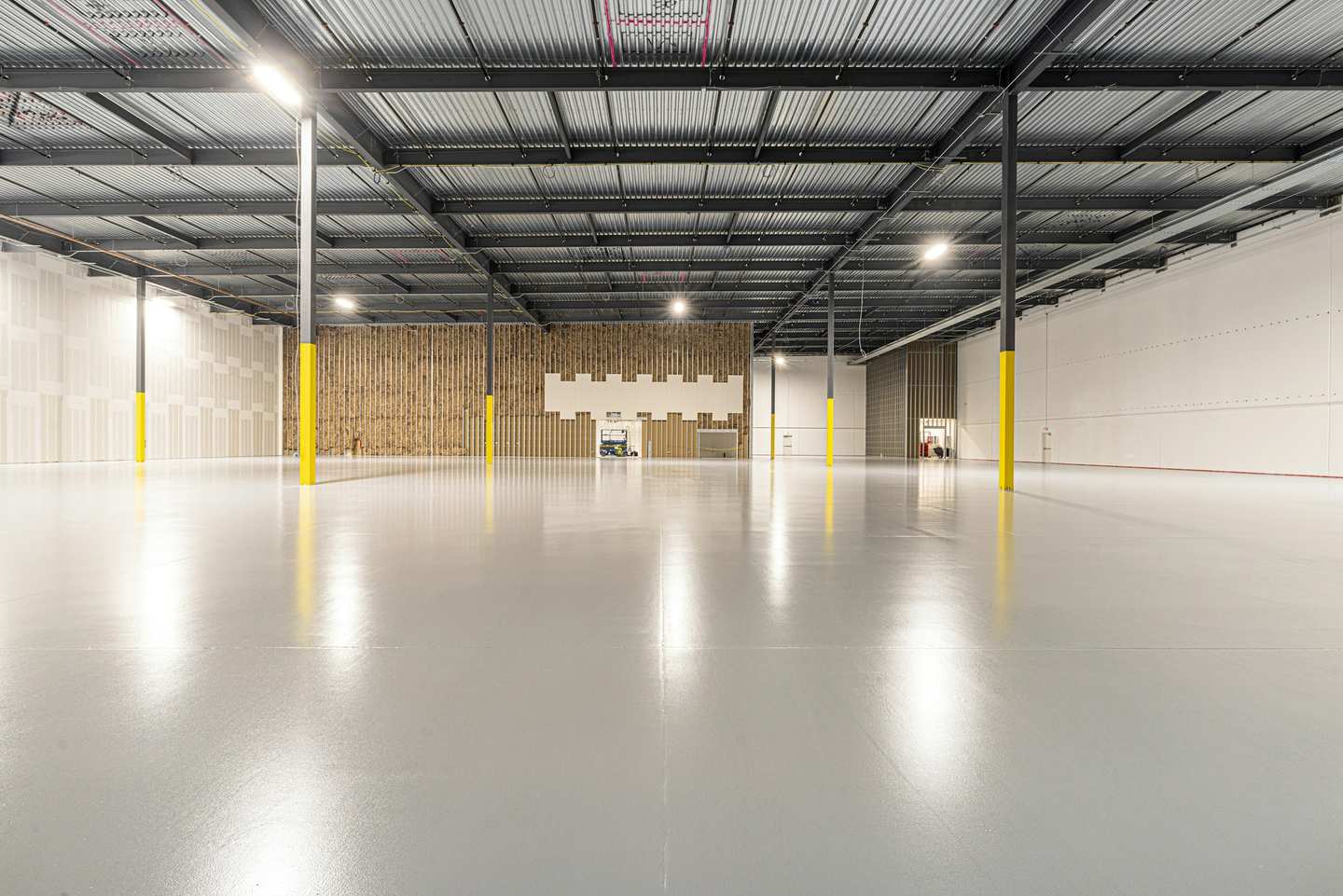 Galpão industrial vazio com piso claro e brilhante e colunas amarelas